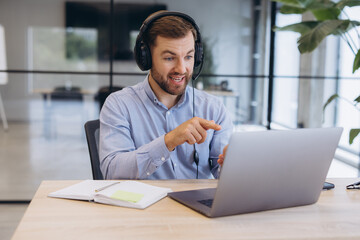 Fototapeta premium Businessman wearing a headset participating in a video call, discussing and pointing at his laptop screen