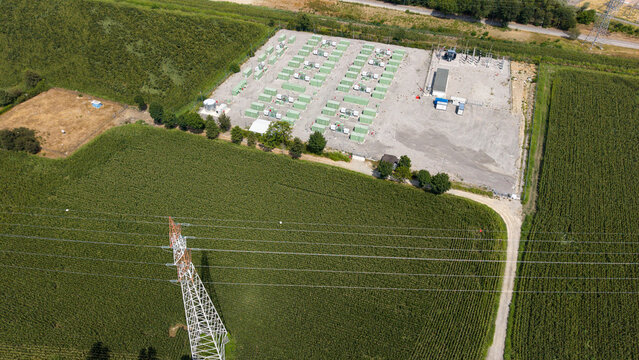 Aerial view of a Battery Energy Storage System with rows of green containers and an electrical substation surrounded by agricultural fields in Tavazzano con Villavesco, Lombardy, Italy.