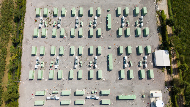 Aerial view of a modern battery energy storage system with rows of green containers and power equipment on a gravel site in Tavazzano con Villavesco, Lombardy, Italy.
