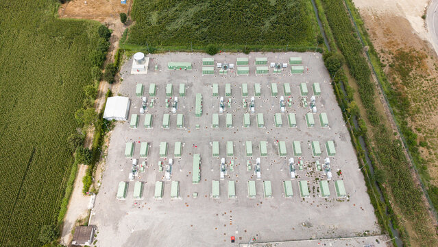 Aerial view of a battery energy storage system with rows of green containers and power grid infrastructure surrounded by agricultural fields in Tavazzano con Villavesco, Lombardy, Italy.