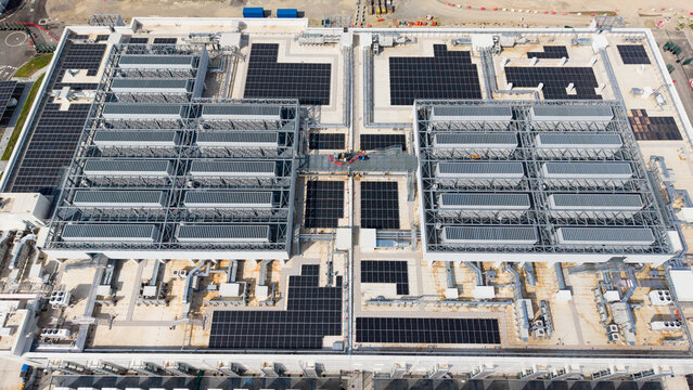 Aerial view of a modern data center campus featuring extensive rooftop solar panel arrays and industrial cooling infrastructure in Melegnano, Lombardy, Italy.