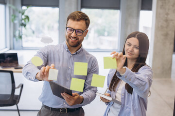 Fototapeta premium Business colleagues collaborating on transparent wall, planning project strategy with sticky notes in modern office