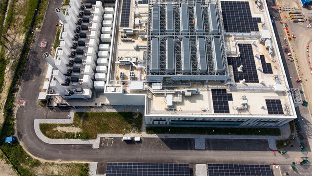 Aerial view of a modern data center campus featuring rooftop solar panels, industrial cooling systems, and paved access roads in Melegnano, Lombardy, Italy.