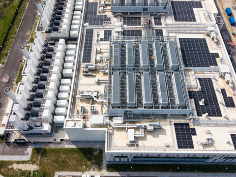 Aerial view of a modern data center campus featuring extensive rooftop solar panels and industrial cooling infrastructure in Melegnano, Lombardy, Italy.