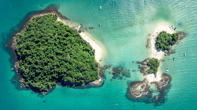 Aerial view of Ilha de Cataguas surrounded by turquoise waters, lush green vegetation, and small boats anchored near the sandy beaches in Angra dos Reis, Rio de Janeiro, Brazil.