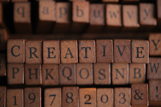 Word CREATIVE in vintage wooden letterpress blocks placed among various printing stamp types.