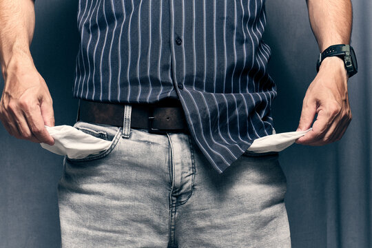 Man pulling out empty pockets from light grey jeans showing concept financial trouble or debt.