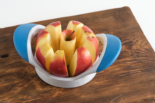 Fresh red apple sliced into pieces with plastic corer on rustic wooden cutting board.