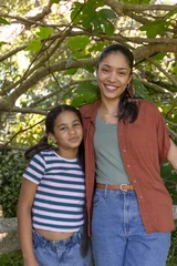 African American mother and youth daughter smiling under leafy canopy in garden, wearing belt © wavebreak3