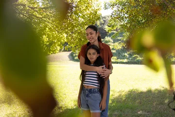 African American mother embracing youth daughter in park under large tree, wearing rust shirt © wavebreak3