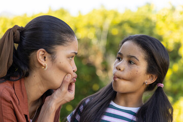 African American woman in rust top pulling cheek, child girl puffing cheeks outdoors, hoop earrings © wavebreak3