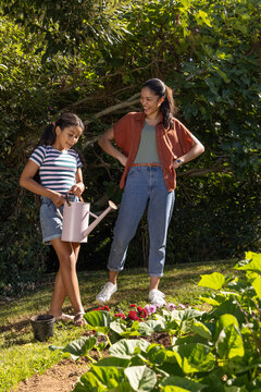 African American mother and daughter in striped tee watering flowers in yard with pink can