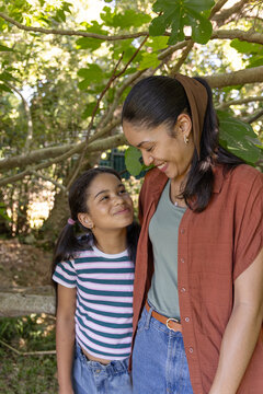 African American mother and daughter child standing in park under canopy by wooden railing, smiling