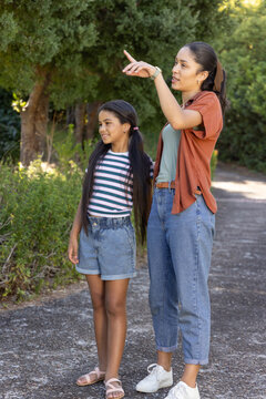 African American mother with child standing on paved path pointing right, wearing watch and shoes