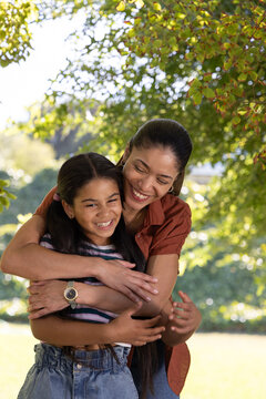African American mother and youth daughter hugging under tree in park showing rust top and watch