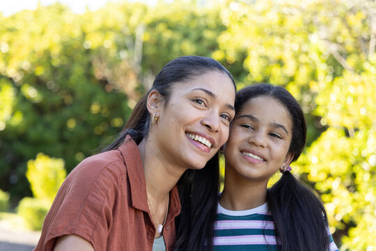 African American mother and youth daughter leaning and smiling in sunlit garden wearing striped tee