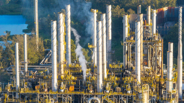 Aerial view of a large petrochemical complex with tall industrial chimneys emitting smoke, intricate piping systems, and surrounding greenery in Santo Andre, State of Sao Paulo, Brazil.