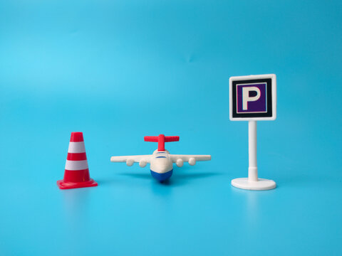 A red traffic cone, a toy airplane, and a parking sign stand arranged on a blue surface