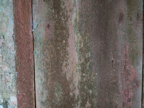 A close-up texture of weathered vertical wooden planks featuring faded red paint and fine cobwebs