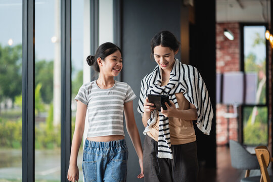Digital Education with two Asian female students walking together and viewing a tablet while smiling in a bright modern classroom learning environment