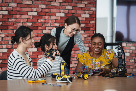 Robotics Education with diverse female teachers and Asian students smiling while exploring robotic hands, electronic equipment, and STEM projects together