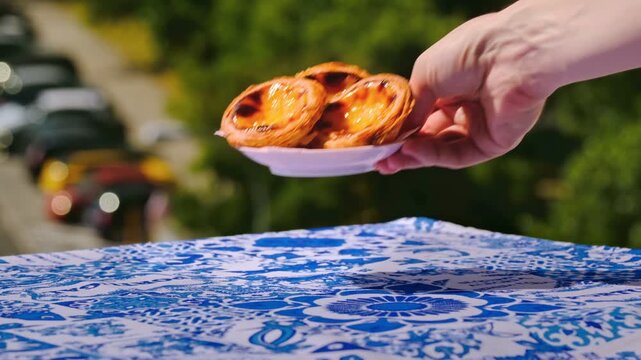 Hand placing three pastel de nata tarts and glass of meia de leite