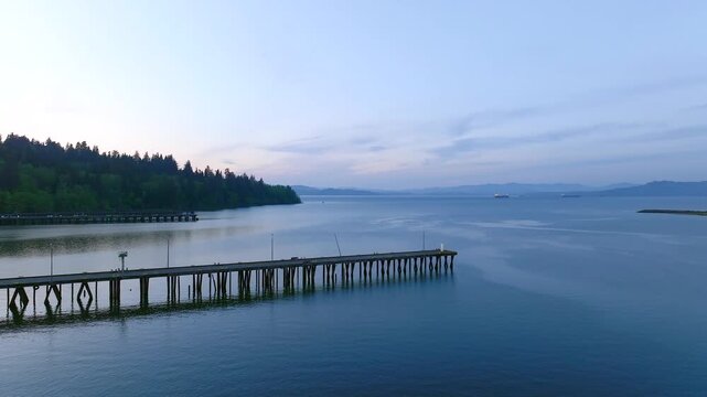 Aerial view of the Columbia River pier extending into the calm water at dusk with forested hills in the background in Astoria, Oregon, United States.
