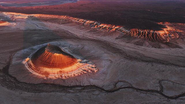 Aerial view of the striped Gora Bokty mountain formation illuminated by golden hour light in the vast desert landscape of Karakiya District, Mangystau Region, Kazakhstan.