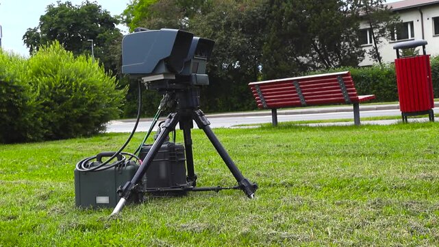 Portable police speed camera on a tripod measuring traffic speed. Automated lidar system controlling vehicle velocity on a roadside to enforce speed limits and improve road safety