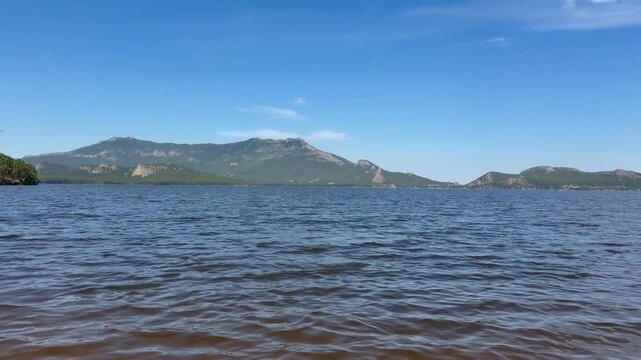 Calm mountain lake with gentle waves and scenic hills in Burabay National Park, Kazakhstan. Peaceful freshwater landscape under a clear blue sky, showcasing the natural beauty of Central Asia