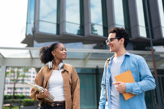 Latino male and African female students walking on campus outdoors. 