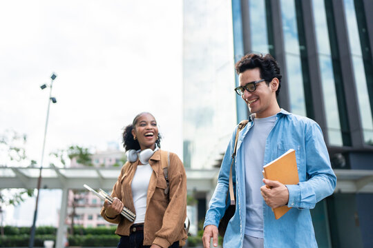 Latino male and African female students walking on campus outdoors. 