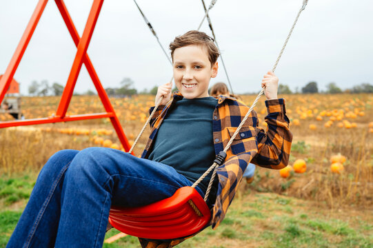 Teen boy enjoying a swing beside a pumpkin patch in autumn