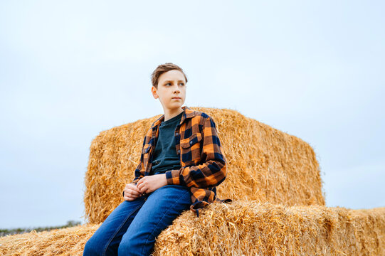 Teen boy sitting on hay bales at a farm during autumn harvest
