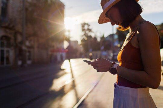 Close-up. a young woman holding a smartphone and typing a message. She is using the phone outdoors against a cityscape background.