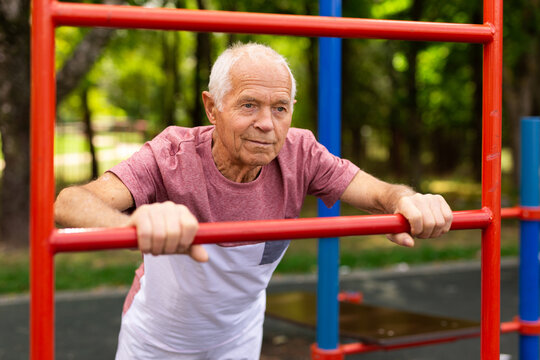 Elderly man doing fitness on sports ground equipment in park