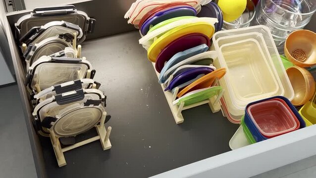 Colorful plastic containers and lids organized in a kitchen drawer, showcasing a neat arrangement with visible dividers and a clean, modern design aesthetic