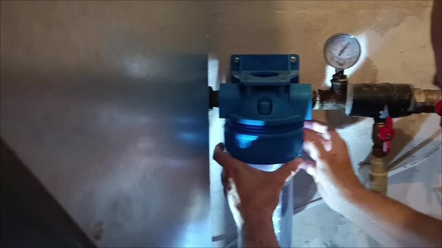 Plumber hands changing water filter cartridge in home system. Maintenance of domestic water filtration unit and pressure gauge.