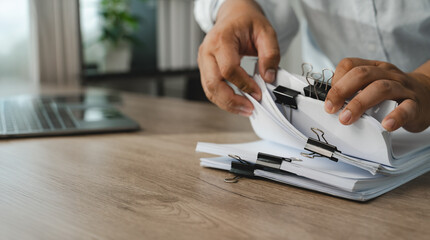 Naklejka na ściany i meble Hands sort clipped paper documents beside laptop on wooden desk, organizing pages and reviewing file bundles for office records management, document handling, filing workflow with copy space.
