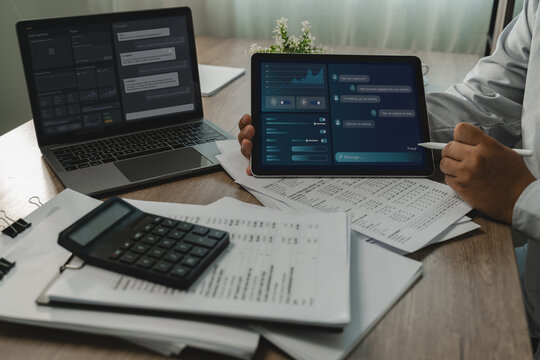 Person uses AI assistant interfaces on a laptop and tablet above paperwork and a calculator, organizing tasks with a stylus and supporting a digital home office workflow at the desk.