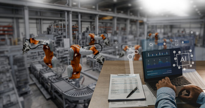 Engineers operate a laptop displaying AI dashboards control graphics in a factory robotic arms, smart industry monitoring, production control, and manufacturing workflow.
