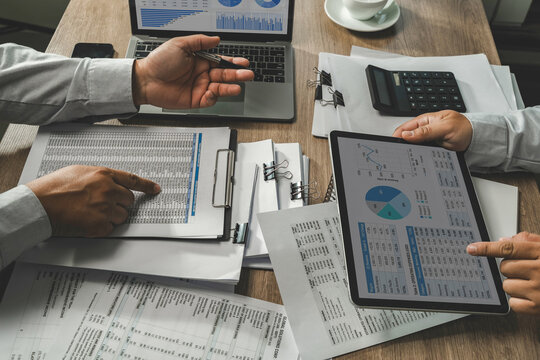 Business people meeting compare financial spreadsheets analyzing with charts on laptop , calculator pens during a desk meeting for data analysis, reporting, and financial review.