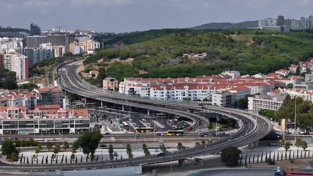 Aerial view of the highway interchange and bus terminal in the town of Alges surrounded by residential buildings and green hills in Alges, Lisbon, Portugal.