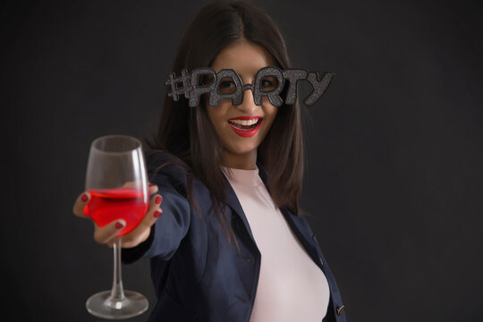 Young woman wearing funky spectacles and holding a wine glass at a party. 