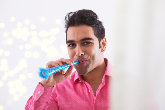 Portrait of a young man with a party blower.