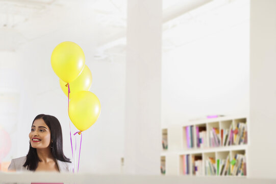 Young woman standing with helium balloons in the office.