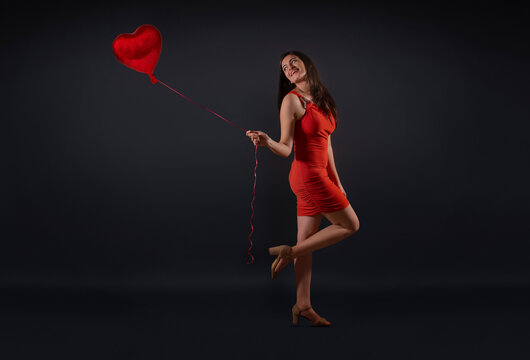Beautiful woman in a party outfit posing with a heart shaped balloon. 