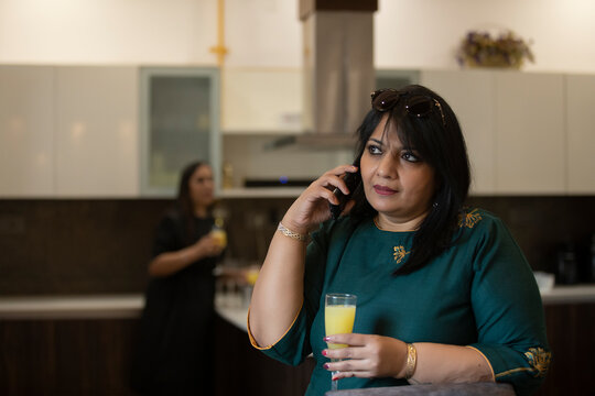 Woman attending a call in Kitchen with drink in her hand.