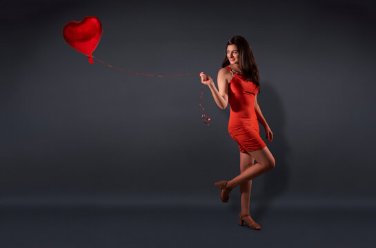Beautiful woman in a party outfit posing with a heart shaped balloon. 