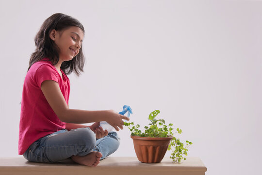 Smiling Young girl spraying plant with water. (Children)  